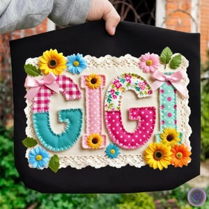 Könnte beinhalten: Schwarze Tragetasche mit dem Namen "GIGI" aus bunten Stoffen appliziert. Die Buchstaben sind mit Blumen, Schleifen und gemusterten Stoffen verziert. Das Design ist mit einem Spitzenrand eingefasst.