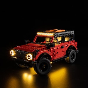 May include: A red toy SUV with black tires and a black roof. The toy car has working headlights and a light bar on the roof. The lights are illuminated, creating a warm glow against the dark background. The toy car is a model of a real SUV.