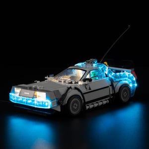Puede incluir: Un modelo de coche DeLorean gris con luces LED azules que iluminan la parte delantera, trasera e interior. El modelo tiene una antena negra y está sobre un fondo negro. Las ruedas del coche son grises.