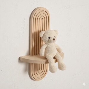 Op de afbeelding: Een lichtgekleurd houten wandplank met een boogvormig ontwerp en een kleine plank. Een cr&egrave;mekleurige teddybeer zit op de plank. De plank is aan een witte muur bevestigd.