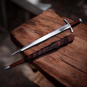May include: A steel sword with a double-edged blade, a straight crossguard, and a brown leather-wrapped handle. Beside it lies a matching brown leather scabbard featuring a dark brown leather strap wrapped in a crisscross pattern around the body.