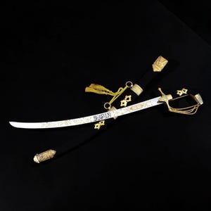 Könnte beinhalten: Ein dekoratives Schwert mit geschwungener Klinge und aufwendigen Golddetails. Das Schwert ist in einer schwarzen Scheide mit goldenen Akzenten untergebracht. Eine goldene Quaste hängt vom Griff. Die Klinge hat arabische Schrift.