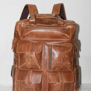 May include: A brown leather backpack with multiple exterior pockets and a top handle. The backpack has adjustable shoulder straps and a zippered main compartment. The leather has a distressed appearance.