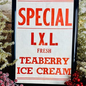 Könnte beinhalten: Ein gerahmtes Vintage-Schild mit den Worten "SPECIAL" und "TEABERRY ICE CREAM" in roten Buchstaben auf cremefarbenem Hintergrund. Das Schild befindet sich in einem schwarzen Rahmen und ist von dekorativen Elementen umgeben.