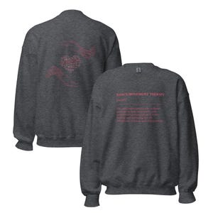 May include: Dark gray sweatshirt with the text "DANCE/MOVEMENT THERAPY (noun)" in pink on the back. The definition of dance movement therapy is also printed in pink. A pink heart and hand design is on the front.