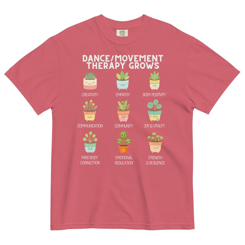 May include: A red t-shirt with the text "DANCE/MOVEMENT THERAPY GROWS" and illustrations of potted plants. Below the text are the words "CREATIVITY", "EMPATHY", "BODY POSITIVITY", "COMMUNICATION", "COMMUNITY", "JOY & VITALITY", "MIND BODY CONNECTION", "EMOTIONAL REGULATION", and "STRENGTH & RESILIENCE".