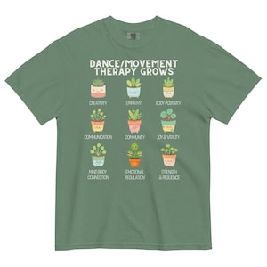 May include: Green t-shirt with the text "DANCE/MOVEMENT THERAPY GROWS" and illustrations of potted plants representing qualities like creativity, empathy, and joy. The shirt is made of a soft, comfortable material.