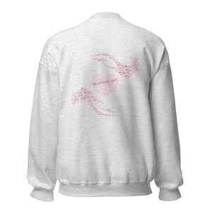 May include: A light gray sweatshirt with a pink graphic on the back. The graphic is a silhouette of a person dancing, composed of words related to dance and movement therapy. The words are in a pink font.