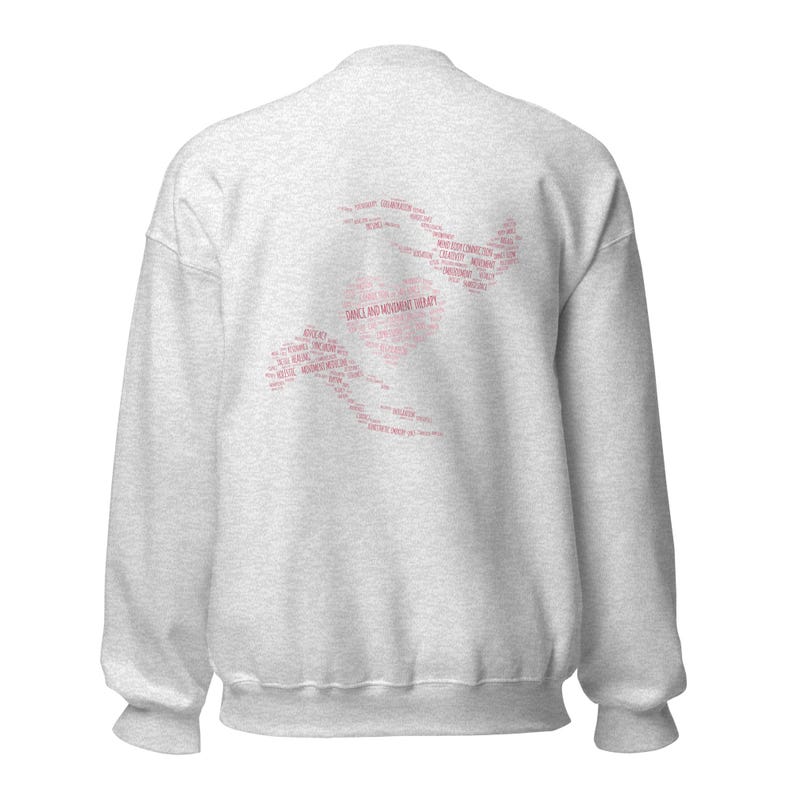 May include: A light gray sweatshirt with a pink graphic on the back. The graphic is a silhouette of a person dancing, composed of words related to dance and movement therapy. The words are in a pink font.
