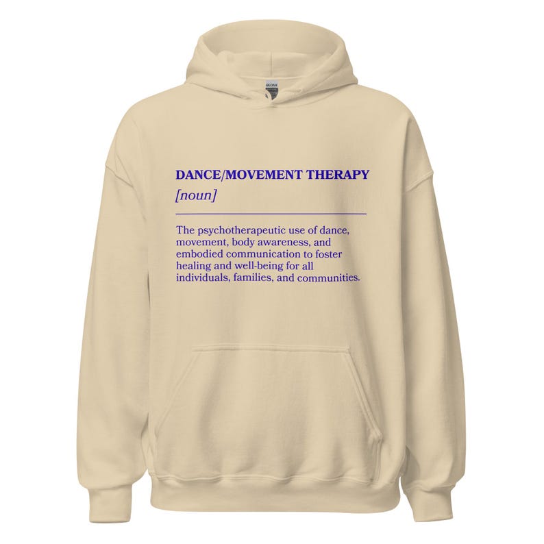 May include: A beige hoodie with a drawstring hood and a front pocket. The front of the hoodie features the text "DANCE/MOVEMENT THERAPY [noun]" in blue, along with a definition of the term.