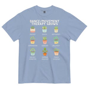 May include: Light blue t-shirt with the text "DANCE/MOVEMENT THERAPY GROWS" and illustrations of potted plants. Each plant represents a positive aspect of dance therapy, such as creativity, empathy, and joy.