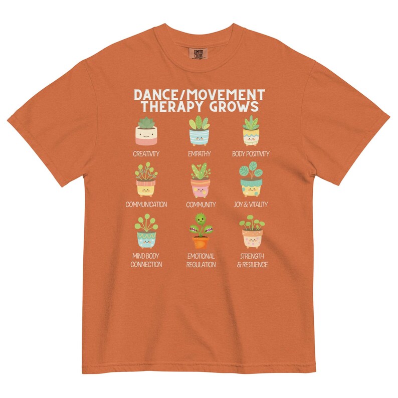 May include: Orange t-shirt with the text "DANCE/MOVEMENT THERAPY GROWS" and illustrations of potted plants. Each plant represents a concept like creativity, empathy, and joy. The shirt is a comfortable fit.