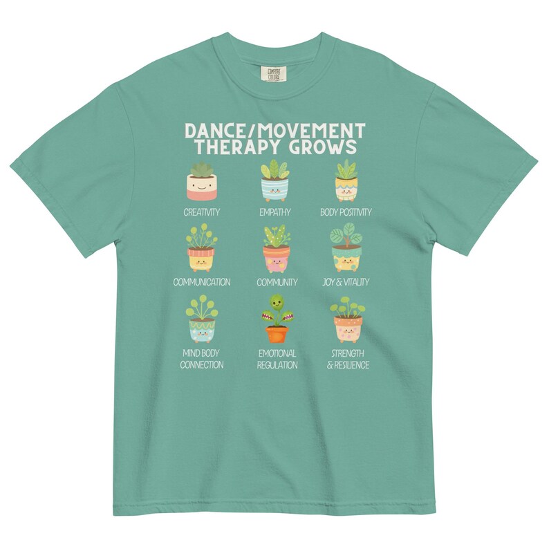 May include: A teal t-shirt with the text "DANCE/MOVEMENT THERAPY GROWS" and illustrations of potted plants representing concepts like creativity, empathy, and body positivity. The shirt is made of a soft material.