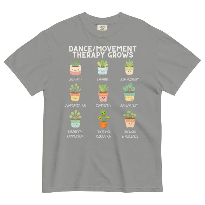 May include: A gray t-shirt with the text "DANCE/MOVEMENT THERAPY GROWS" in white. Below the text are nine colorful illustrations of potted plants, each labeled with a positive concept like "Creativity" and "Empathy".