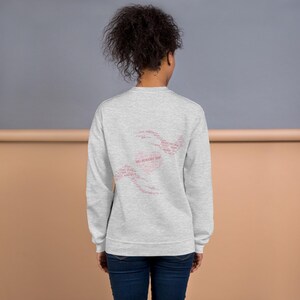 May include: A light gray sweatshirt with a pink heart-shaped design on the back, composed of various words. The sweatshirt is a crew neck style and is made of a soft material. The text in the heart shape reads "WILL RECOVER HEART".
