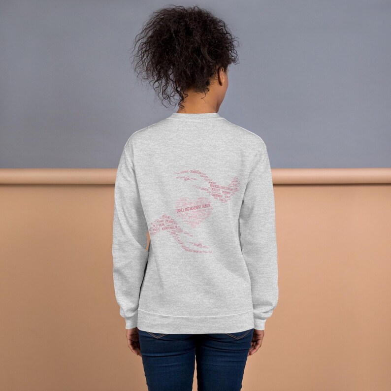 May include: A light gray sweatshirt with a pink heart-shaped design on the back, composed of various words. The sweatshirt is a crew neck style and is made of a soft material. The text in the heart shape reads "WILL RECOVER HEART".