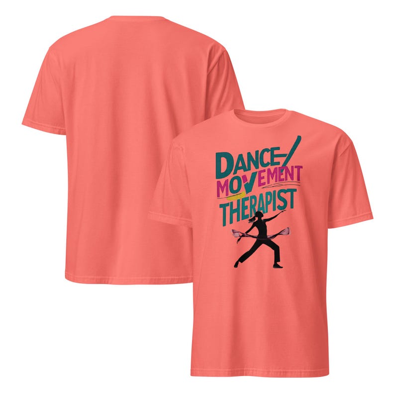 May include: Coral-colored t-shirts. One shirt displays the text "DANCE MOVEMENT THERAPIST" in teal, pink, and yellow, with a black silhouette of a person holding two objects. The second shirt is a solid coral color.