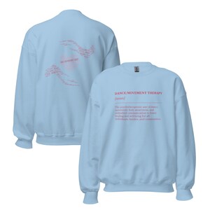May include: Light blue sweatshirt with the text "DANCE/MOVEMENT THERAPY [noun]" in pink. The back of the sweatshirt has a pink design with the words "DANCE AS MOVEMENT THERAPY". The sweatshirt is a crew neck.