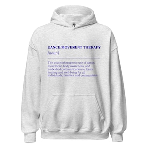 May include: A light gray hoodie with a front pocket and a drawstring hood. The front of the hoodie features the text "DANCE/MOVEMENT THERAPY [noun]" in blue, along with a definition of the term. The hoodie is made of a soft material.