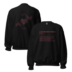 May include: Black sweatshirt with the text "DANCE/MOVEMENT THERAPY [noun]" in pink. The back of the sweatshirt features a heart and hands design in pink. The text describes the psychotherapeutic use of dance for healing and well-being.
