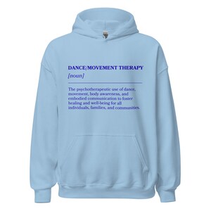 May include: A light blue hoodie with the text "DANCE/MOVEMENT THERAPY [noun]" in blue. The text below describes the psychotherapeutic use of dance, movement, body awareness, and embodied communication to foster healing and well-being.