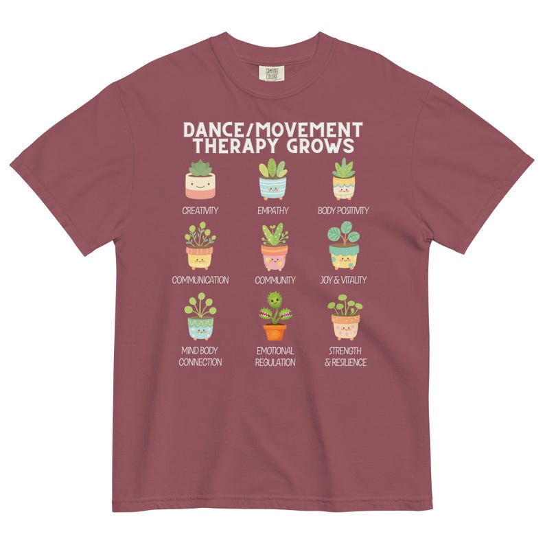 May include: A maroon t-shirt featuring the text "DANCE/MOVEMENT THERAPY GROWS" above illustrations of potted plants. Each plant represents a concept like creativity, empathy, and joy & vitality. The shirt is made of a soft, comfortable material.