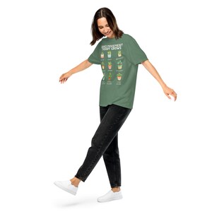 May include: A green t-shirt with the text "DANCE/MOVEMENT THERAPY GROWS" and illustrations of various potted plants. The person is wearing black jeans and white shoes.