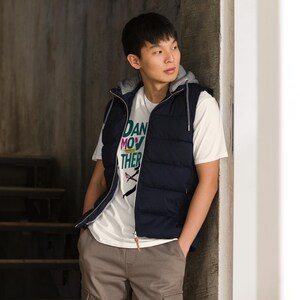 May include: A navy blue hooded vest with a light gray lining is worn over a white t-shirt. The t-shirt features the text "DAN MOV THER" in colorful letters. The person is wearing brown cargo pants.