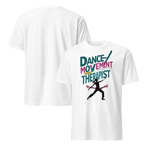 May include: White t-shirt featuring the text "DANCE MOVEMENT THERAPIST" in teal, magenta, and yellow. A black silhouette of a dancer is below the text, holding pink ribbons. The back of the shirt is plain white.