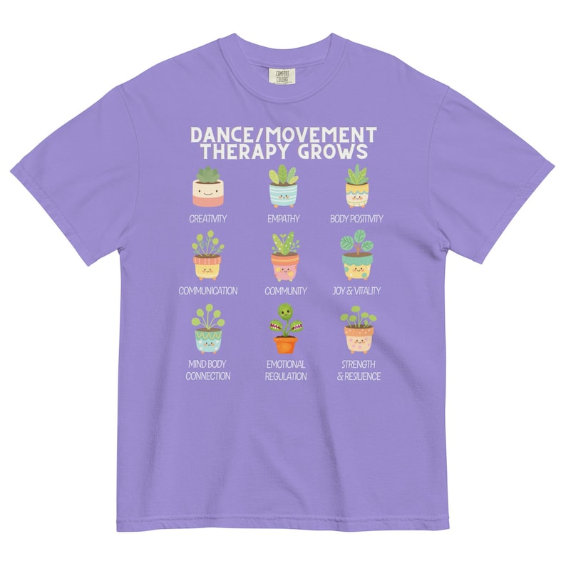 May include: A lilac-colored t-shirt featuring the text "DANCE/MOVEMENT THERAPY GROWS" above illustrations of potted plants. Each plant represents a positive concept such as creativity, empathy, and body positivity. The shirt is made of a soft material.