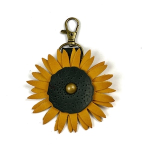 May include: A leather sunflower keychain with a gold-toned clasp. The sunflower is yellow with a dark green center and a gold-toned button.