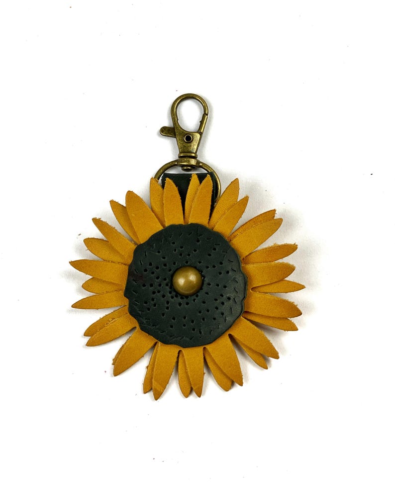May include: A leather sunflower keychain with a gold-toned clasp. The sunflower is yellow with a dark green center and a gold-toned button.