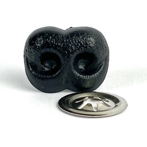 May include: Black plastic dog nose with two nostrils and a textured surface. The nose comes with a silver metal fastener.