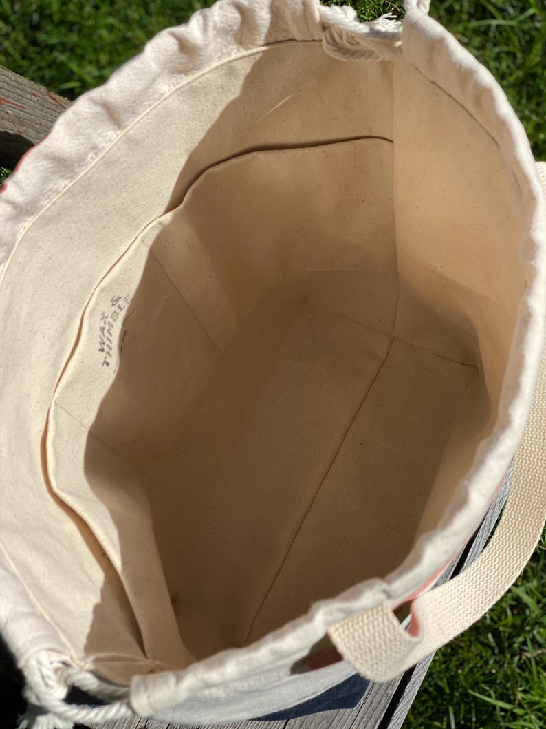 May include: A white canvas tote bag with a drawstring closure and a single strap. The bag has a small pocket on the inside and the text "WAY & THING" is printed on the inside of the bag.