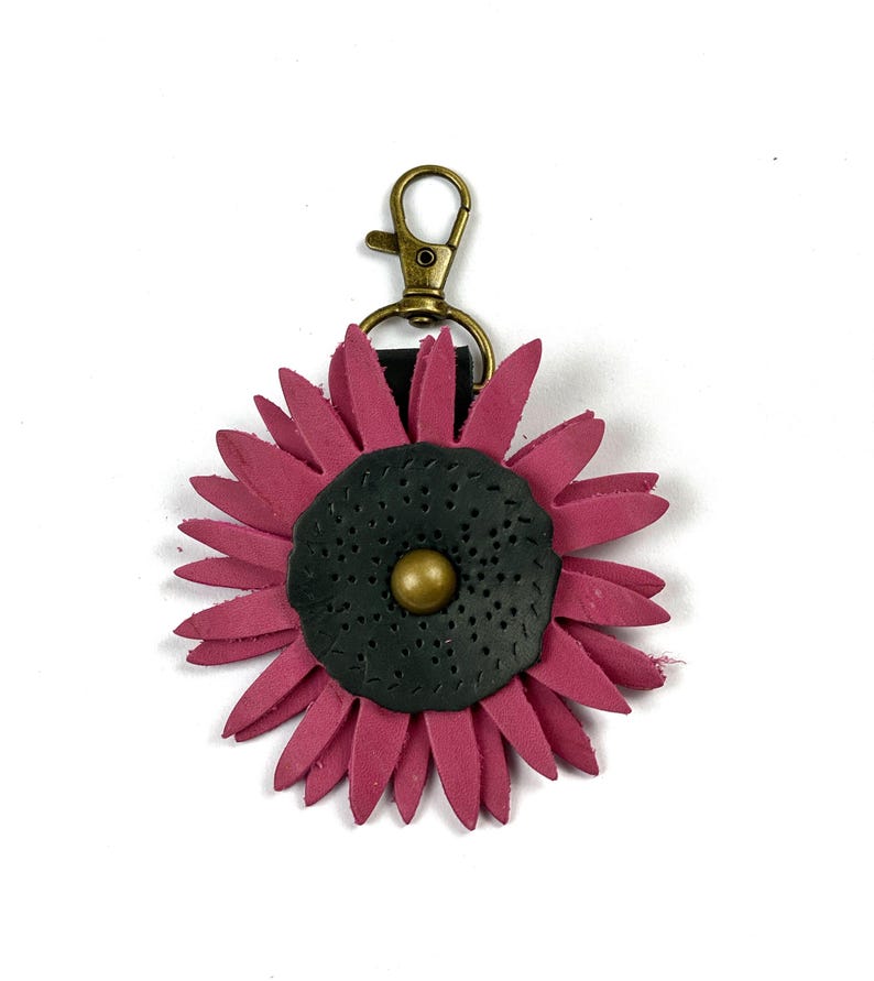 May include: A pink leather flower keychain with a black center and a gold button. The keychain has a brass clasp.