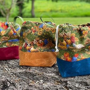 May include: Three drawstring bags with a rooster and sunflower print. The bags have different colored bottoms: burgundy, brown, and blue.