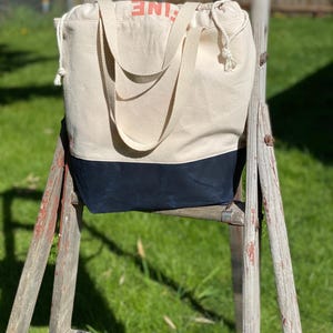 May include: A white canvas tote bag with black trim and the word "LINE" printed in orange on the front. The bag is sitting on a wooden ladder.