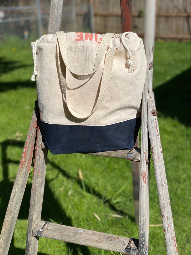 May include: A white canvas tote bag with black trim and the word "LINE" printed in orange on the front. The bag is sitting on a wooden ladder.