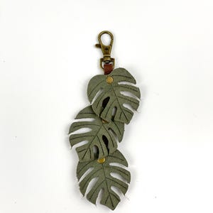 May include: A green leather keychain with three monstera leaves attached to a brass key ring.