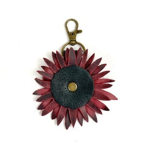 May include: A burgundy leather sunflower keychain with a black center and a gold metal clasp.