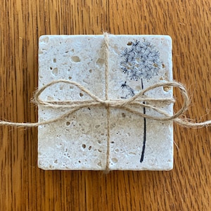 May include: Set of four beige stone coasters with a black dandelion design. The coasters are tied together with twine.