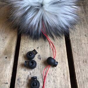 May include: Four black plastic toggle stoppers with a red cord. The stoppers have a spring mechanism and are used for securing cords or straps.