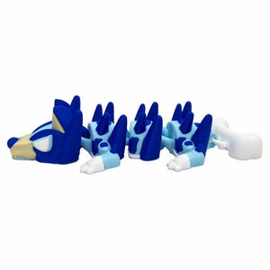 May include: A blue and light blue articulated toy dog with a bone-shaped tail. The toy dog has a segmented body with dark blue spikes along its back. The head is blue with tan and white accents.