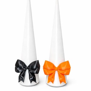 May include: Two white, cone-shaped decorative objects, each adorned with a satin bow. One bow is black, the other is bright orange. The objects are set against a white background.