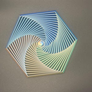 Könnte beinhalten: Ein geometrisches Wandkunstwerk in sechseckiger Form. Das Kunstwerk zeigt ein Spiraldesign mit Schichten aus blauen, grünen und gelben Farbtönen. Das Stück hat einen dreidimensionalen Effekt, der Tiefe und visuelles Interesse erzeugt.