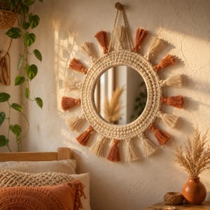 May include: A round wall mirror featuring a thick, cream-colored macrame frame with a textured knot pattern. The mirror is decorated with alternating cream and terracotta-colored yarn tassels arranged in a sunburst pattern around the perimeter.