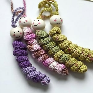 May include: Four handmade crochet caterpillar ornaments in purple, pink, green, and yellow. Each caterpillar has a smiling wooden bead head with pink cheeks. The crochet bodies are detailed and textured, with a loop for hanging.