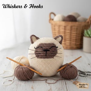 Puede incluir: Un juguete con forma de gato tejido a ganchillo en crema y marrón, con una cara sonriente y bigotes. La imagen incluye ovillos de lana, ganchillos y el texto "Whiskers & Hooks". Una etiqueta dice "Handmade with Love".