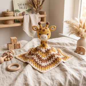 Op de afbeelding: Een gehaakt giraf-knuffeldoekje met een geel en bruin opgevuld girafhoofd bevestigd aan een vierkante deken in een granny square-patroon in tinten crème, mosterdgeel en bruin met een geschulpte crèmekleurige rand.