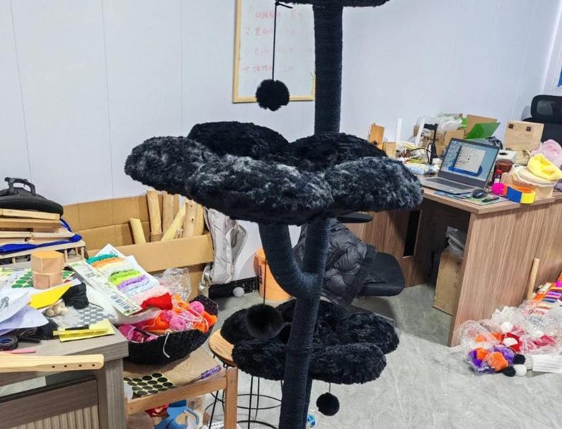 May include: A black cat tree with multiple levels and a central scratching post. The platforms are covered in a soft, plush material. The cat tree has a sturdy base and several dangling pom-poms for play.